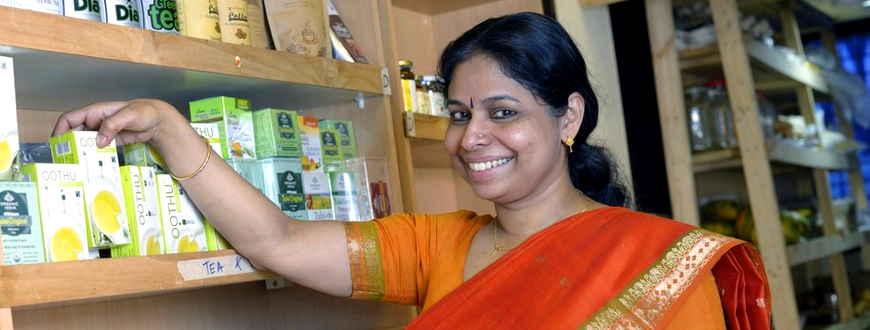 Eine Kundin in einem indischen Bioladen betrachtet das Angebot an Fairtrade-Tees und lächelt in die Kamera.